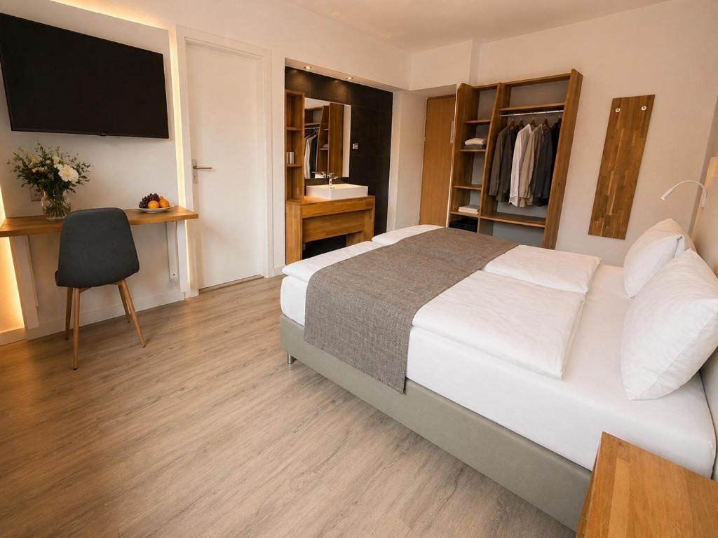 Modernes Economy-Doppelzimmer im Hotel Drei Könige in Chur, mit einem komfortablen Bett mit grauem Bettläufer, einem offenen Kleiderschranksystem aus Holz, einem integrierten Waschtisch und hellem Parkettboden.
