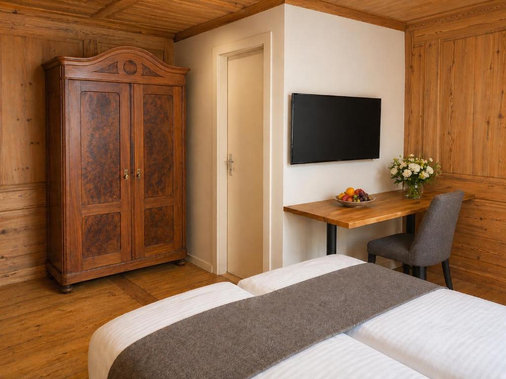 Traditionelles historisches Hotelzimmer im Hotel Drei Könige mit kunstvoller, edler Holzvertäfelung an Wänden und Decke, einem großen antiken Holzschrank, einem Flachbildfernseher und einem Schreibtisch aus Holz.