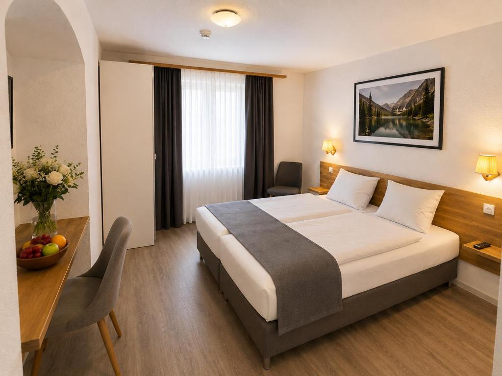 Gemütliches und einladendes Standard-Doppelzimmer im Hotel Drei Könige in Chur, mit makellos weißer Bettwäsche, einem minimalistischen hölzernen Kopfteil, integrierten Nachttischen und einem Schreibtisch.