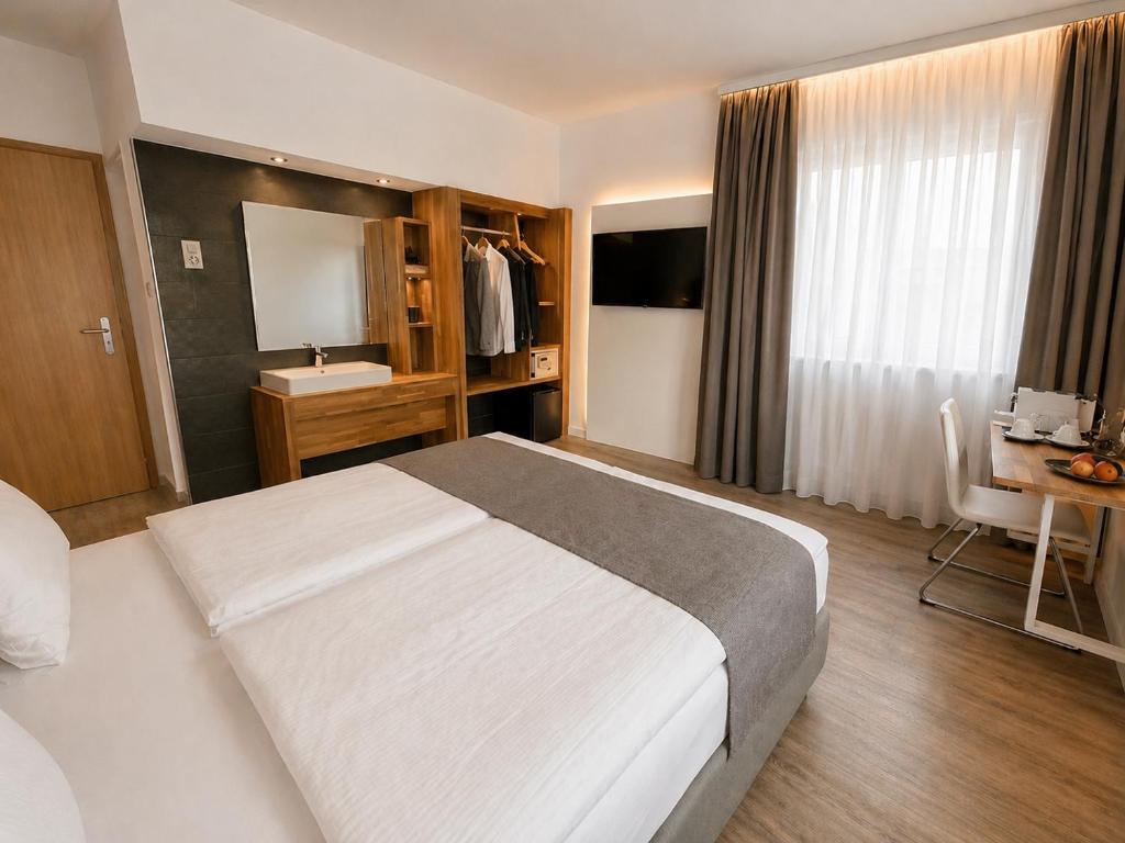 Premium-Superior-Doppelzimmer im Hotel Drei Könige in Chur, mit einem komfortablen Bett mit grauem Läufer, einem maßgefertigten, offenen Holzschrank, einem integrierten Waschtisch und einem Schreibtisch am Fenster.